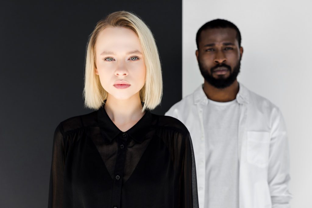 african american boyfriend and blonde girlfriend looking at camera near black and white wall