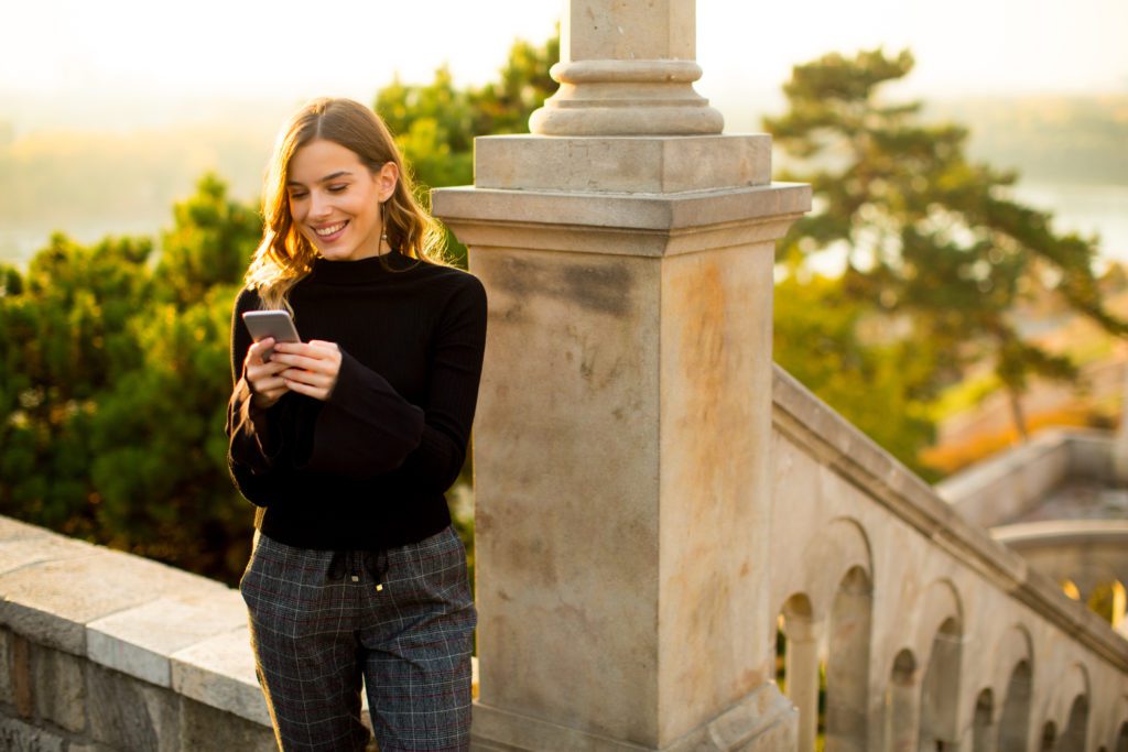 Young woman holding mobile phone while standing on the old stairs in the park